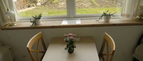 A room with a window, a desk, two chairs, and a potted plant on the windowsill.