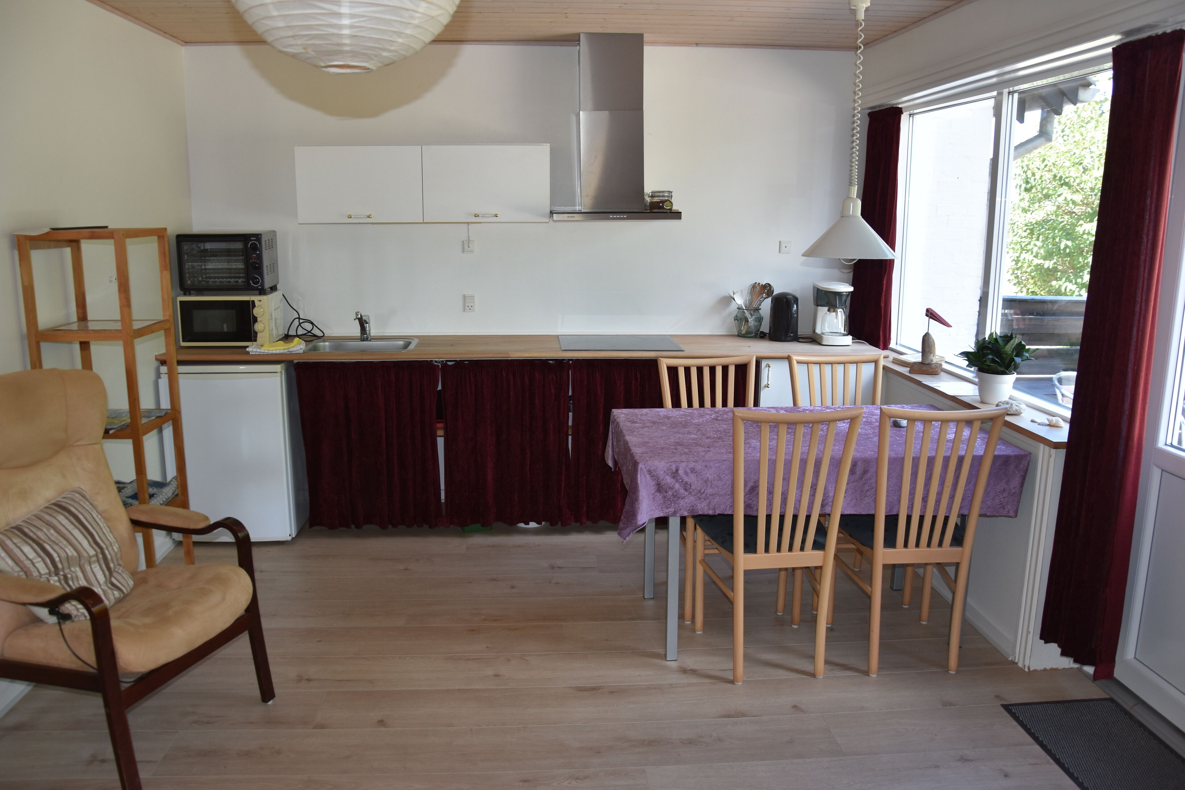 A compact kitchen with a dining area, wooden chairs, a small table, and a window with curtains.