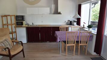 Una cocina compacta con zona de comedor, sillas de madera, una mesita y una ventana con cortinas.