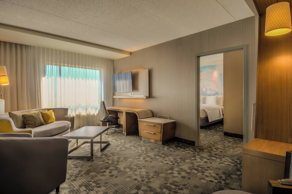 Ein Hotelzimmer mit Sofa, Schreibtisch, Stuhl, Nachttisch, Lampe und Bett.