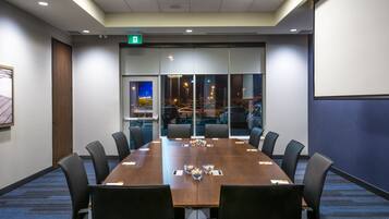 Un salón de conferencias con una larga mesa, sillas y una pantalla para proyector.
