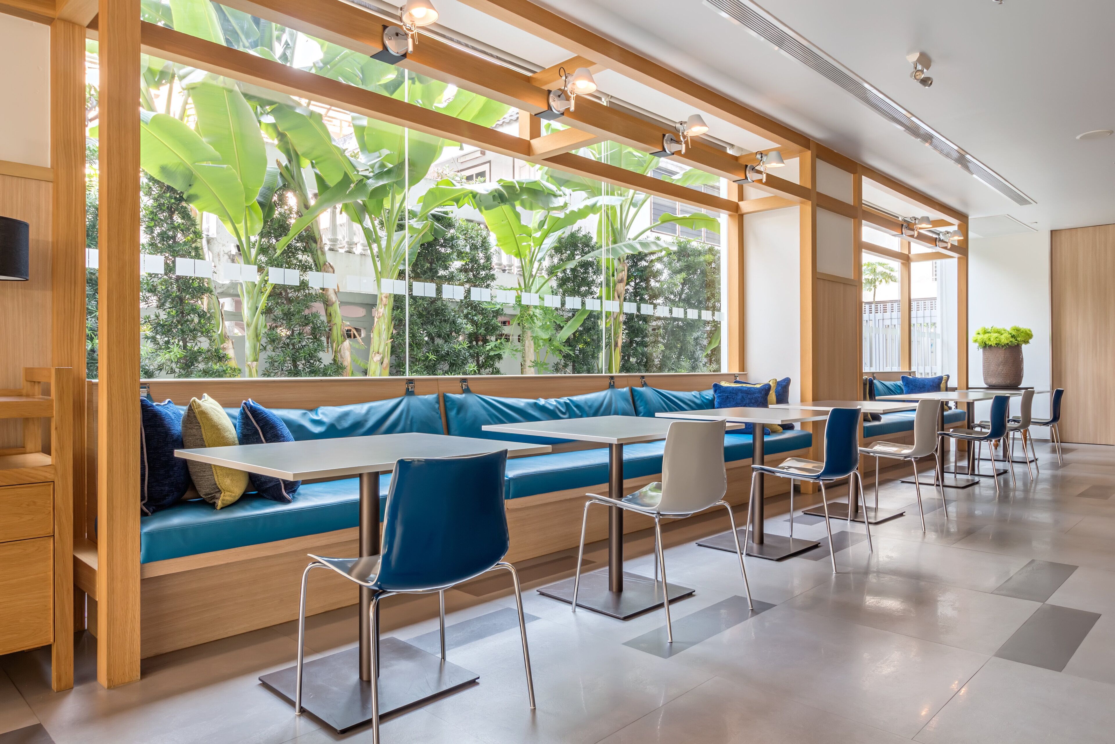Un espace de détente intérieur moderne, avec des poutres en bois, des bancs rembourrés bleus et des chaises en métal.