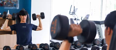 A gym with a person lifting dumbbells, various weight plates, and exercise equipment.