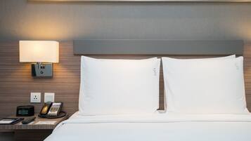 A hotel room with a bed, a bedside lamp, a phone, and a clock.