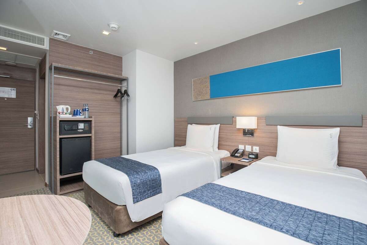 A hotel room with two beds, a desk, a mini-fridge, and a coffee maker.