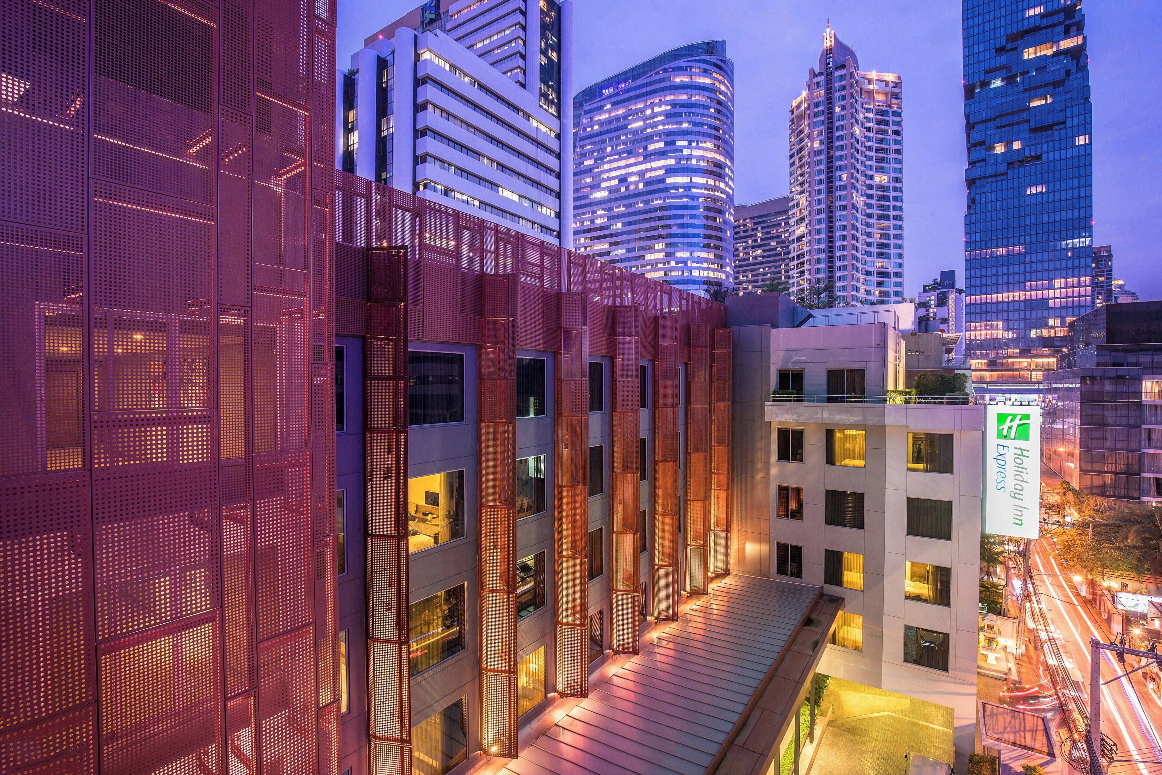 A modern hotel with a glass facade, multiple floors, and a rooftop terrace.
