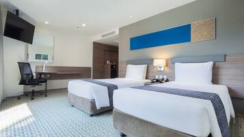 A hotel room with two beds, a desk, a chair, and a flat-screen TV.