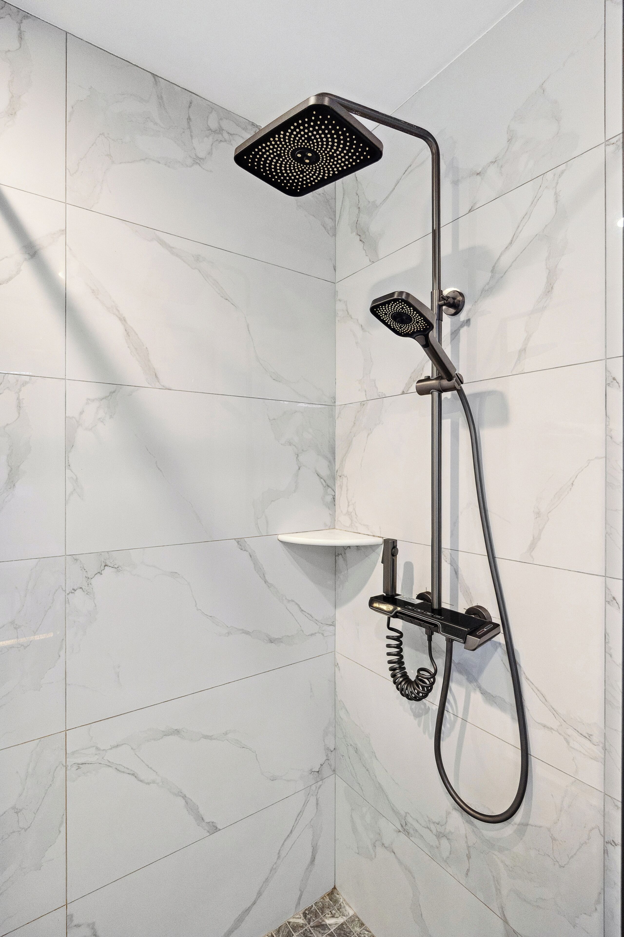 A modern shower with a handheld showerhead and a fixed showerhead mounted on the wall.