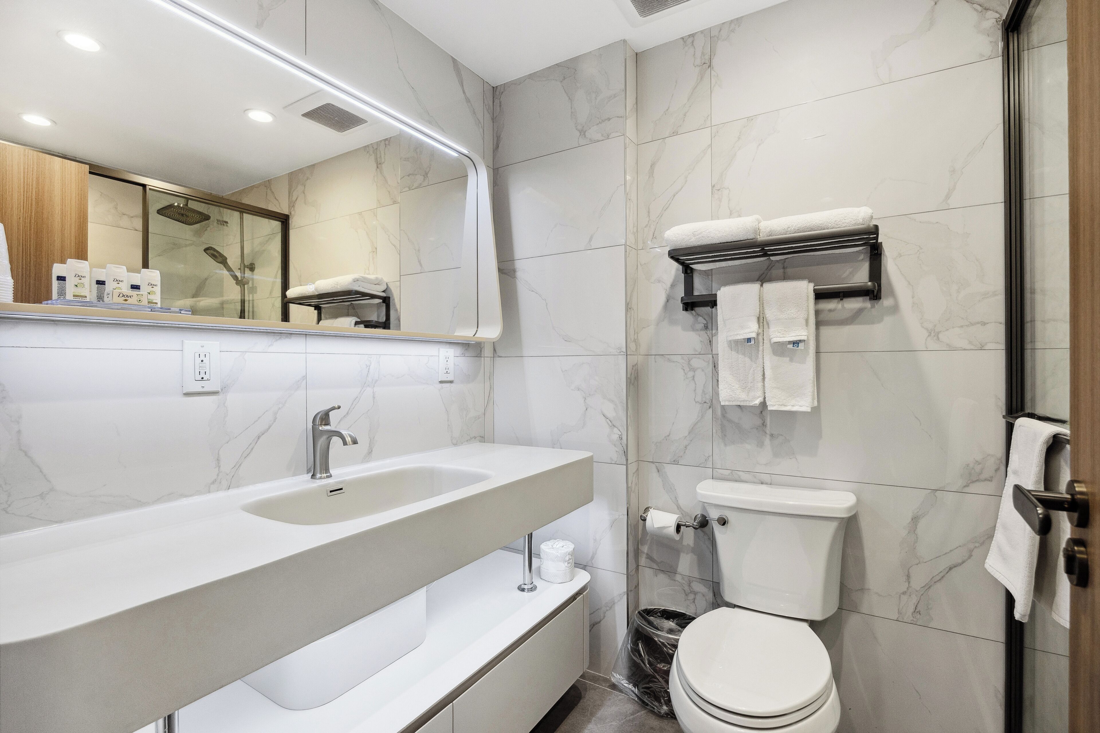 A modern bathroom with a marble backsplash, a large sink, a toilet, and a shower area.