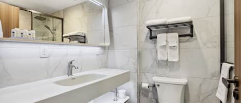 A modern bathroom with a marble backsplash, a large sink, a toilet, and a shower area.