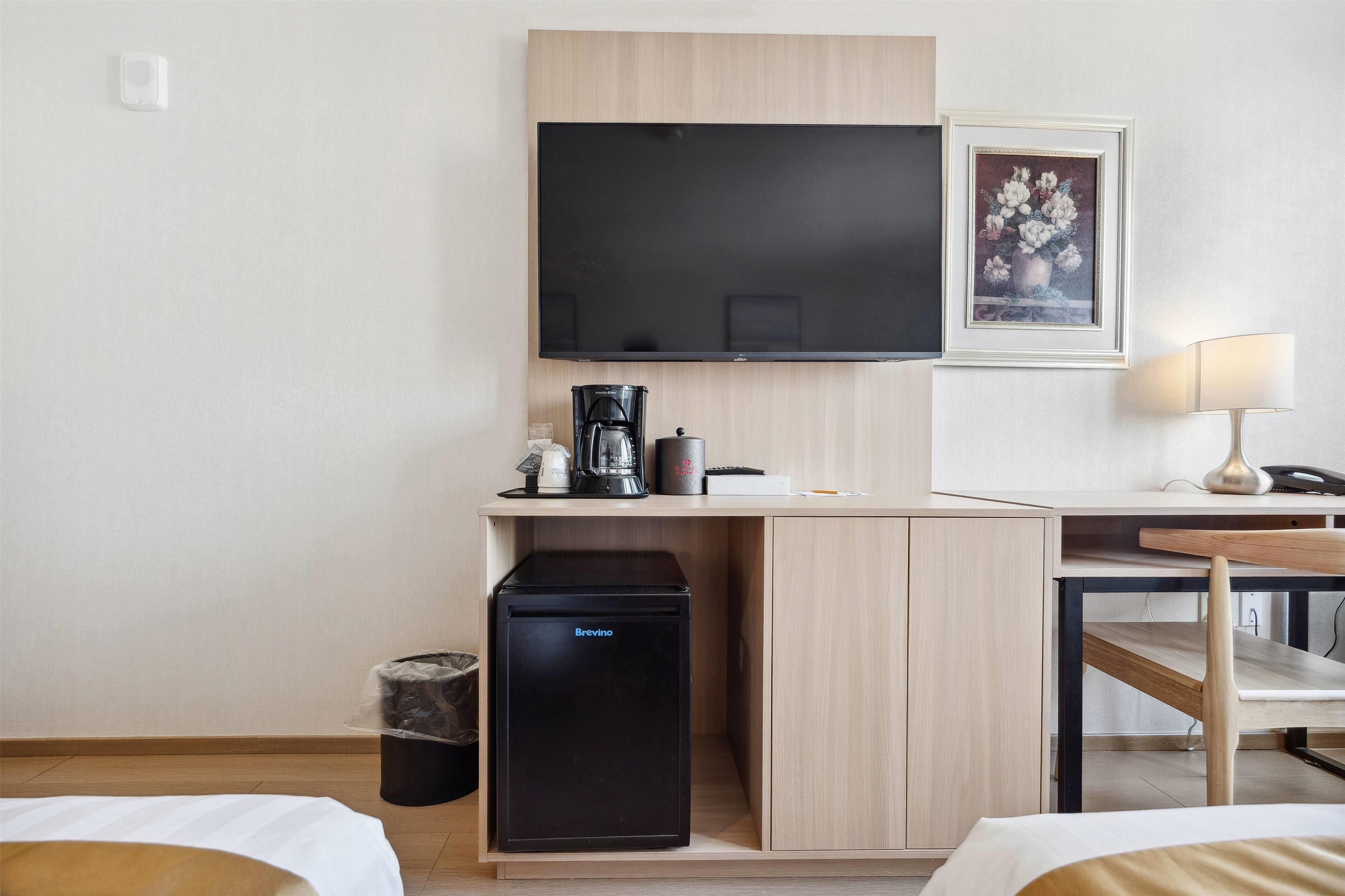 Quarto de hotel com cozinha compacta, televisão de tela plana, obra de arte floral emoldurada e abajur.
