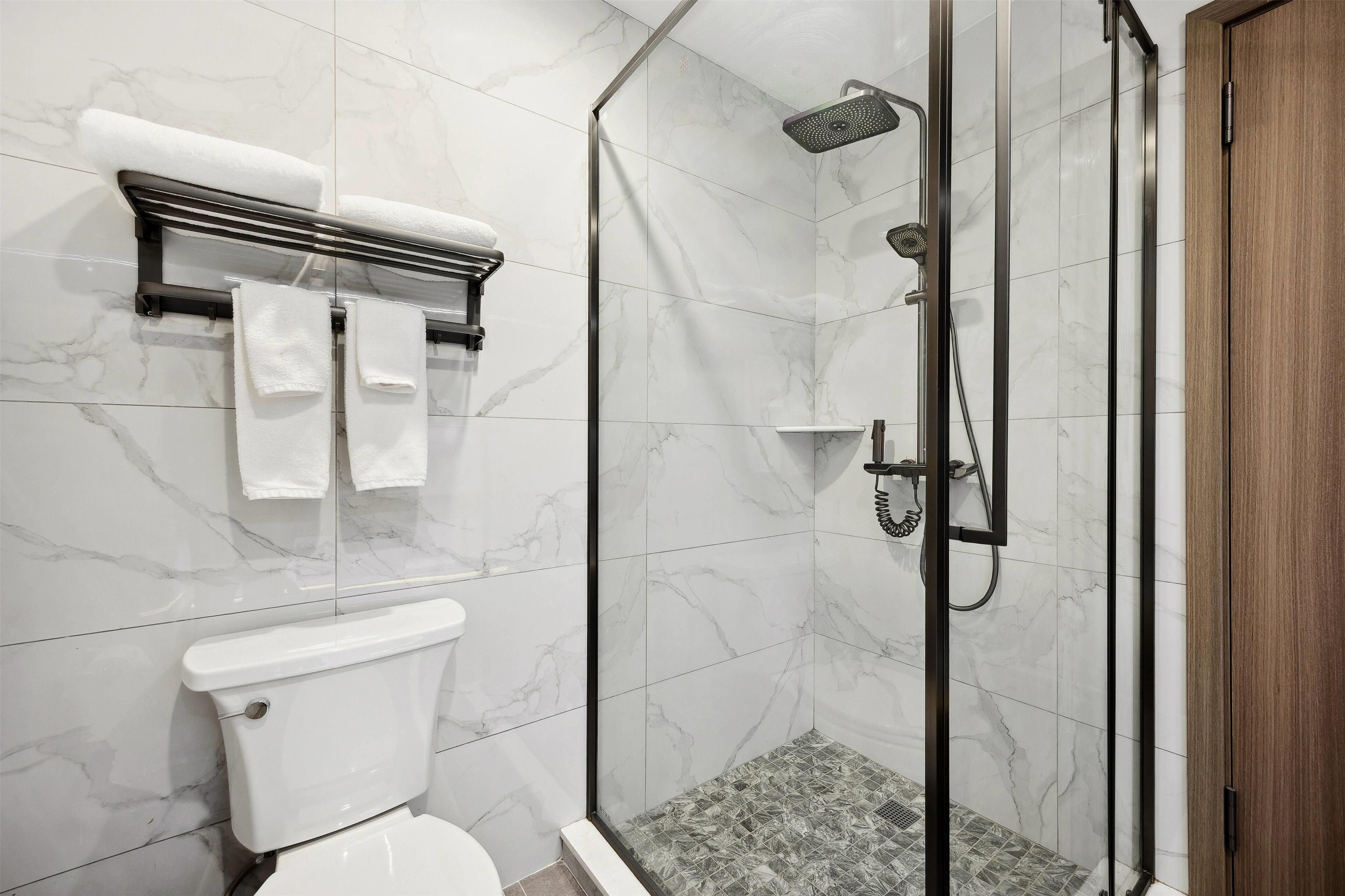 A modern bathroom with a glass-enclosed shower, a toilet, and a towel rack with towels.