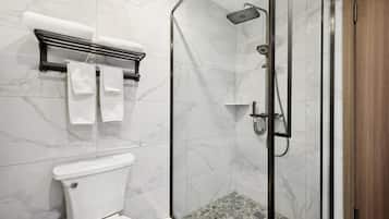 A modern bathroom with a glass-enclosed shower, a toilet, and a towel rack with towels.