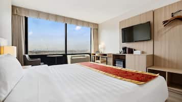 A hotel room with a large bed, a desk, a chair, a TV, and a window with a city view.