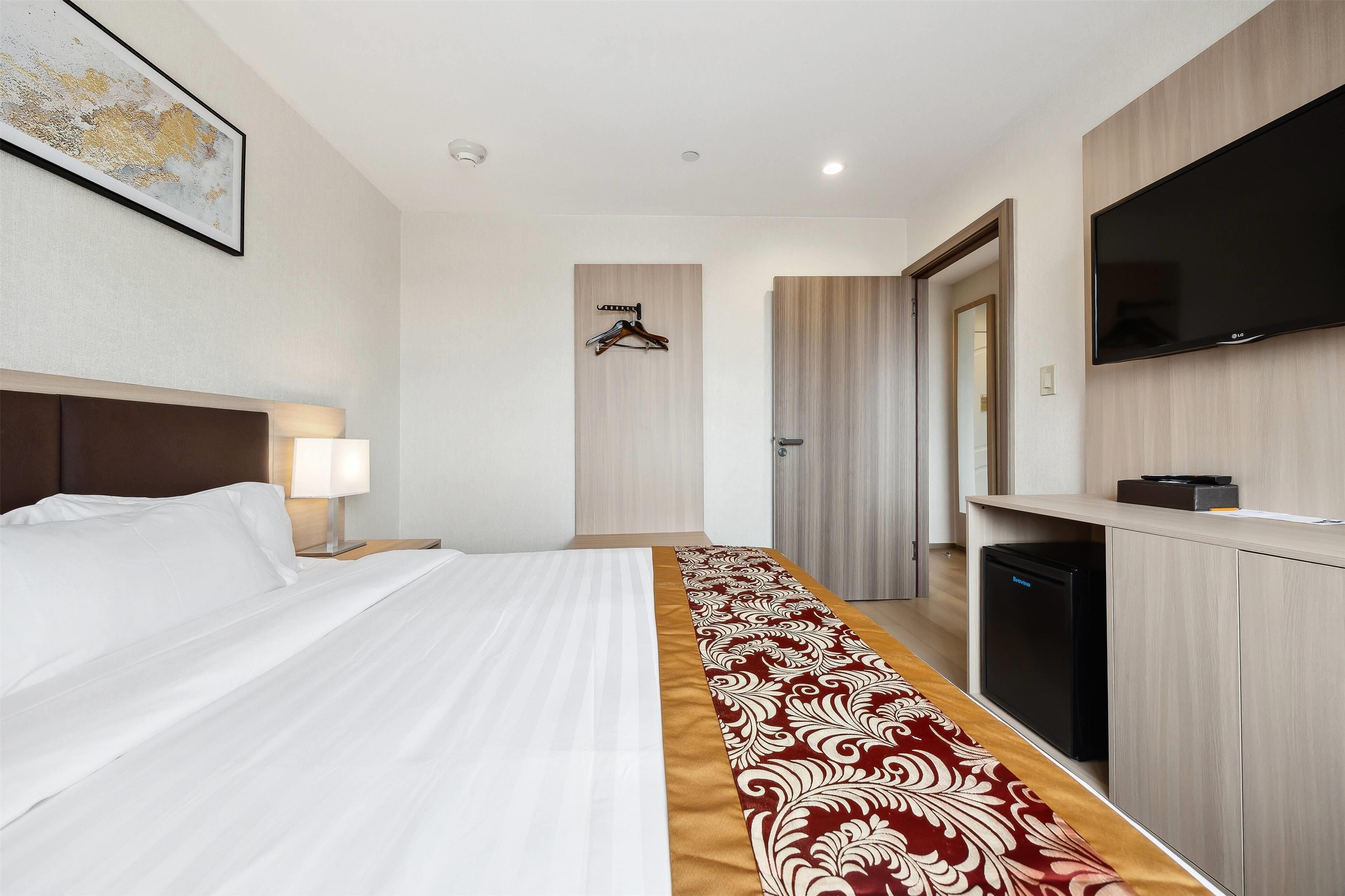 A hotel room with a bed, a desk, a television, and a wardrobe.