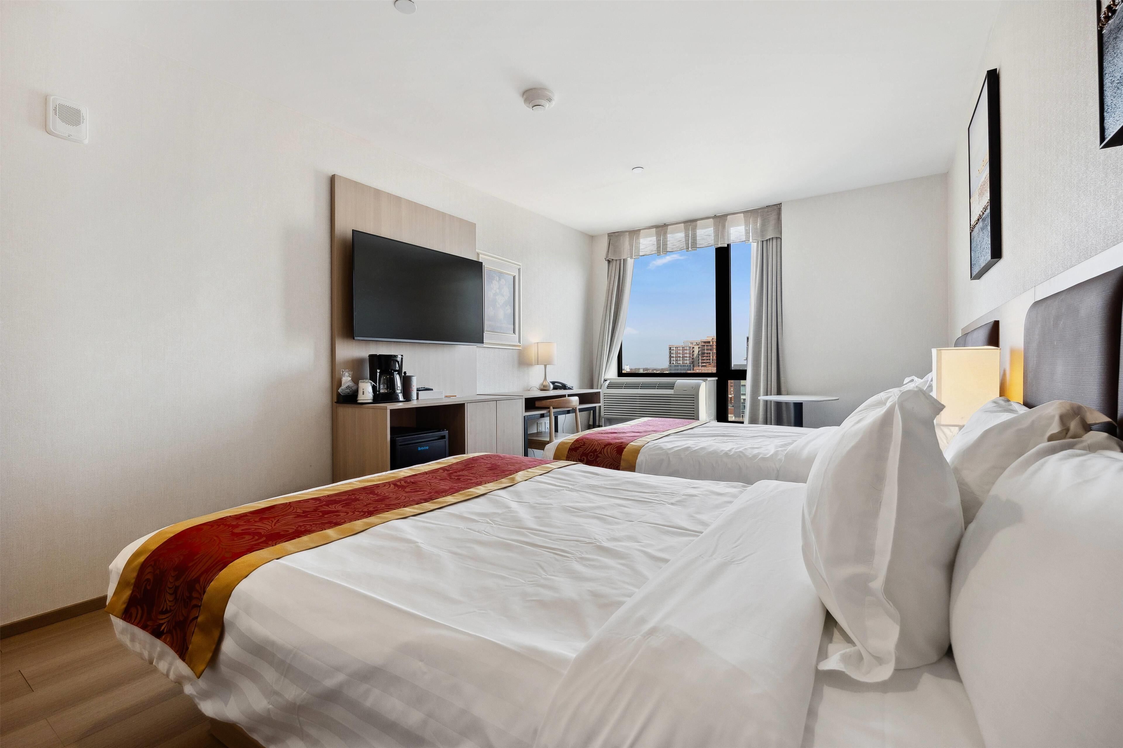 Ett hotellrum med två sängar, en TV, ett skrivbord med en kaffebryggare och utsikt över staden.