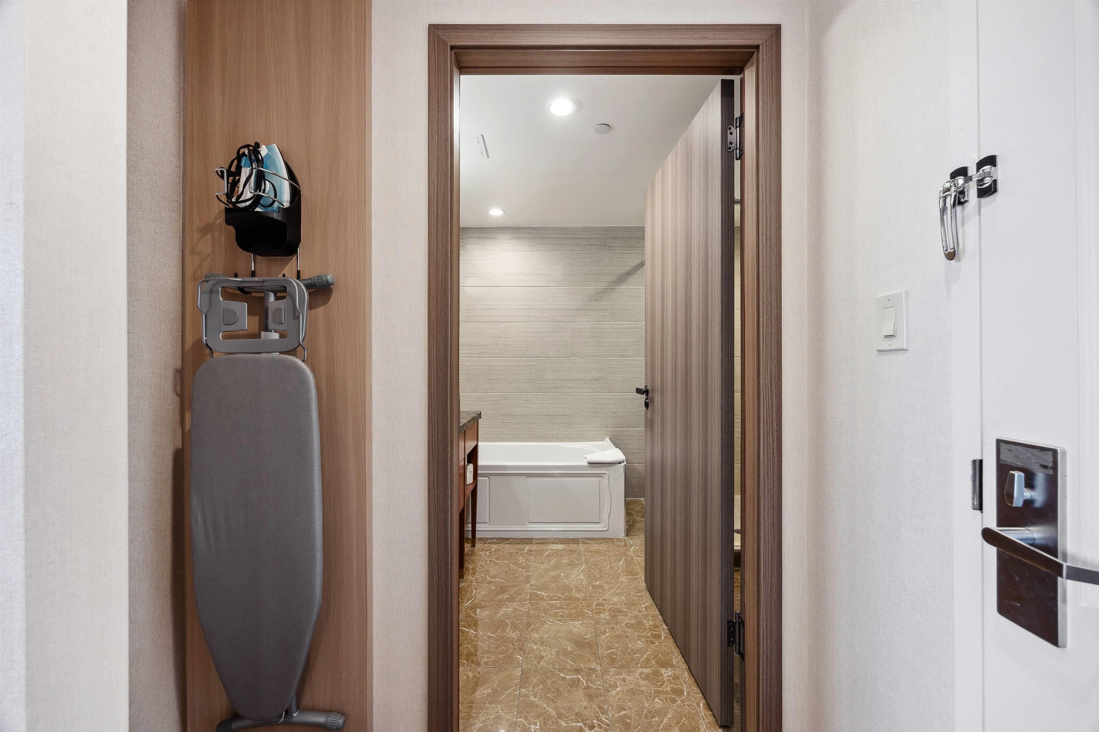 A hotel hallway with a wooden door, a white bathtub, and a towel rack.
