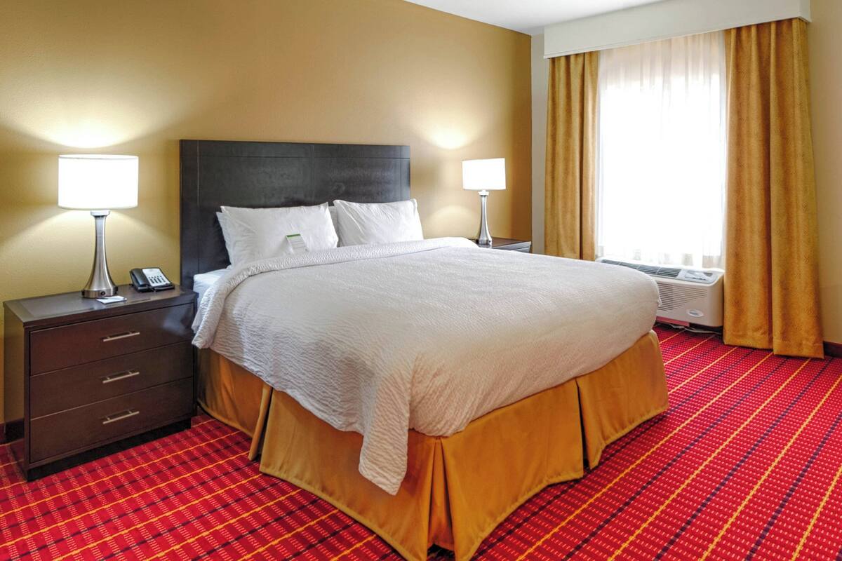 A hotel room with a large bed, two bedside tables with lamps, a heater, and a window with curtains.