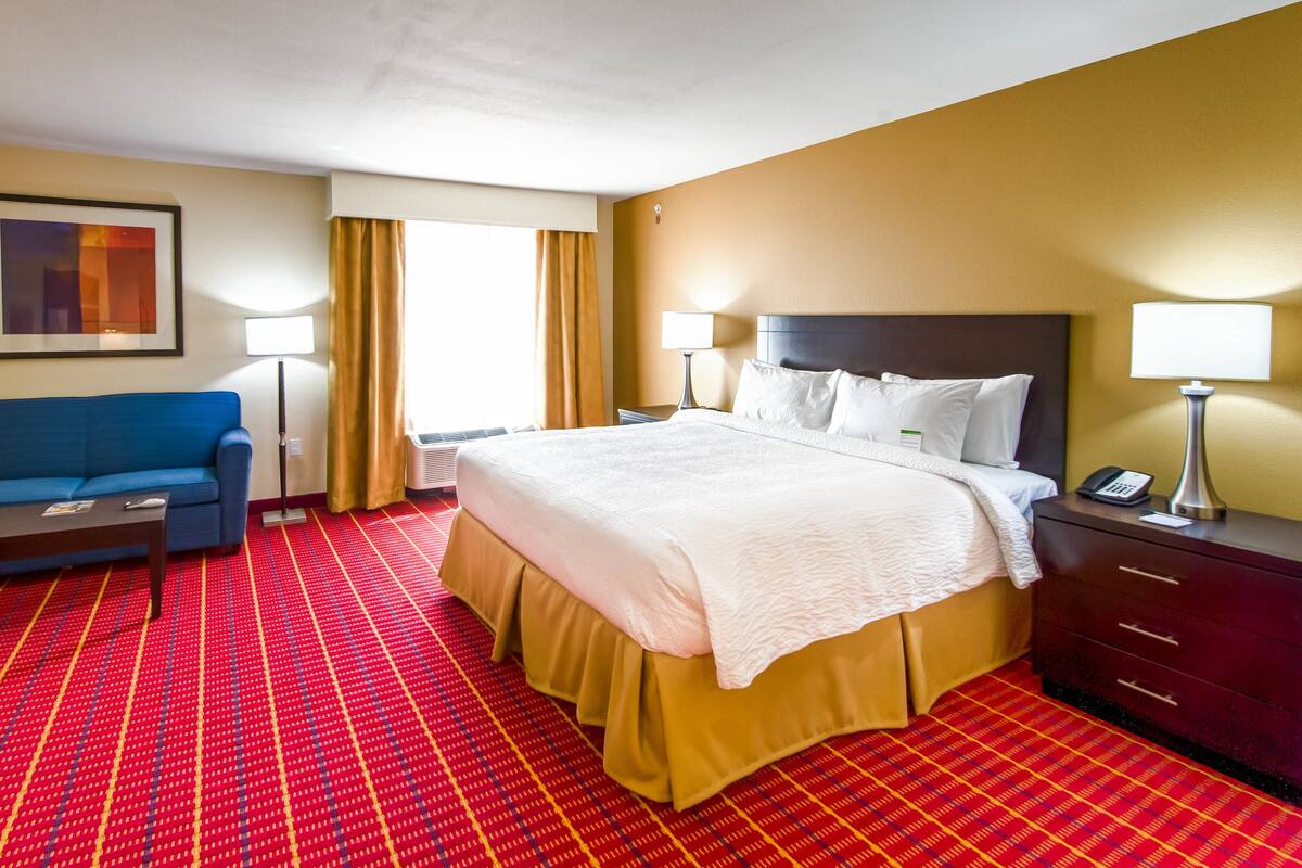 A hotel room with a large bed, a blue sofa, a small table, and a desk with a lamp.