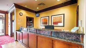 A hotel reception area with a wooden reception desk, a clock, and framed artwork on the wall. - TownePlace Suites El Paso Airport (El Paso)