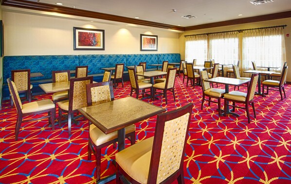 Uma área de refeições de hotel com cabines e mesas, carpete estampado e obras de arte emolduradas nas paredes.