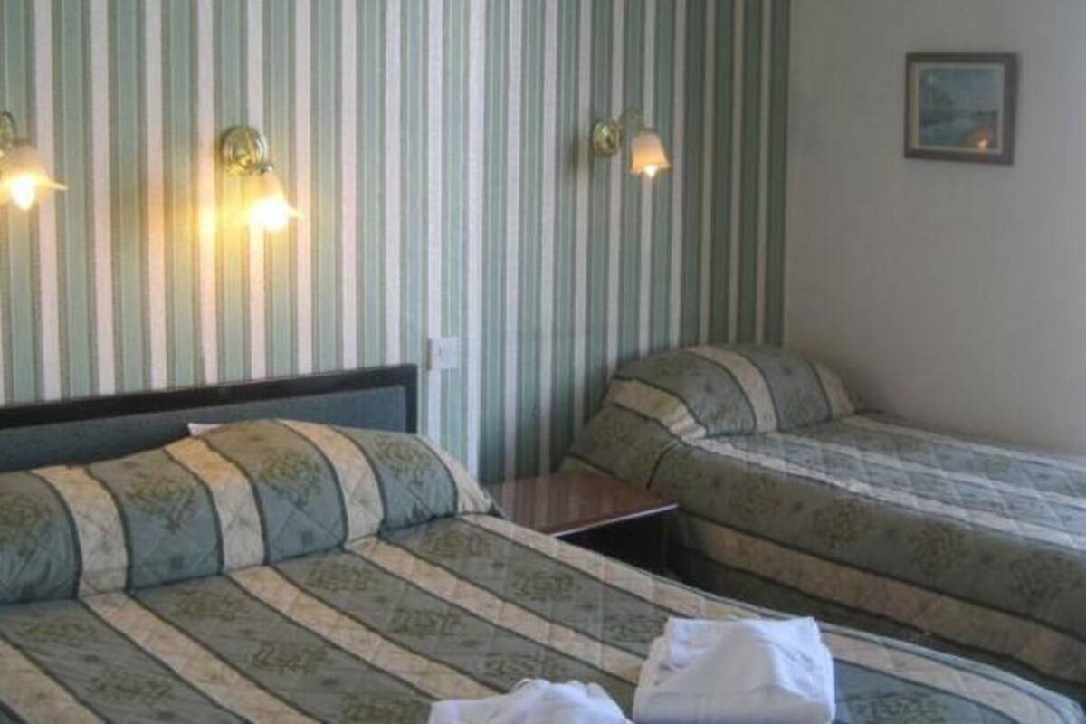 Una habitación con dos camas, papel tapiz a rayas, lámparas fijadas a la pared y un pequeño cuadro.