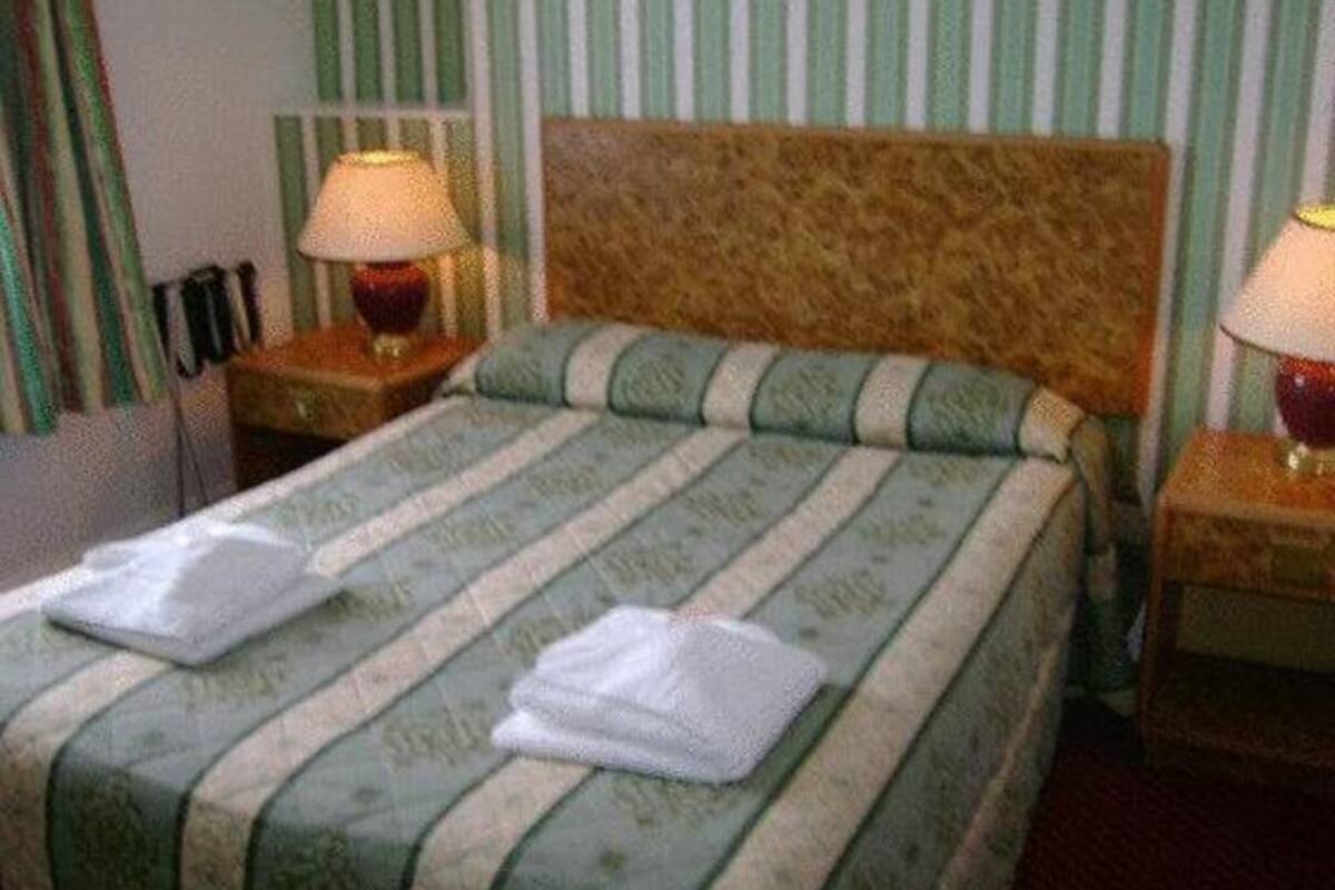 Una habitación de hotel con una cama, dos lámparas de noche y una pared a rayas.