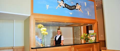 A reception desk with a "Welcome" sign, a receptionist, and a floral arrangement.