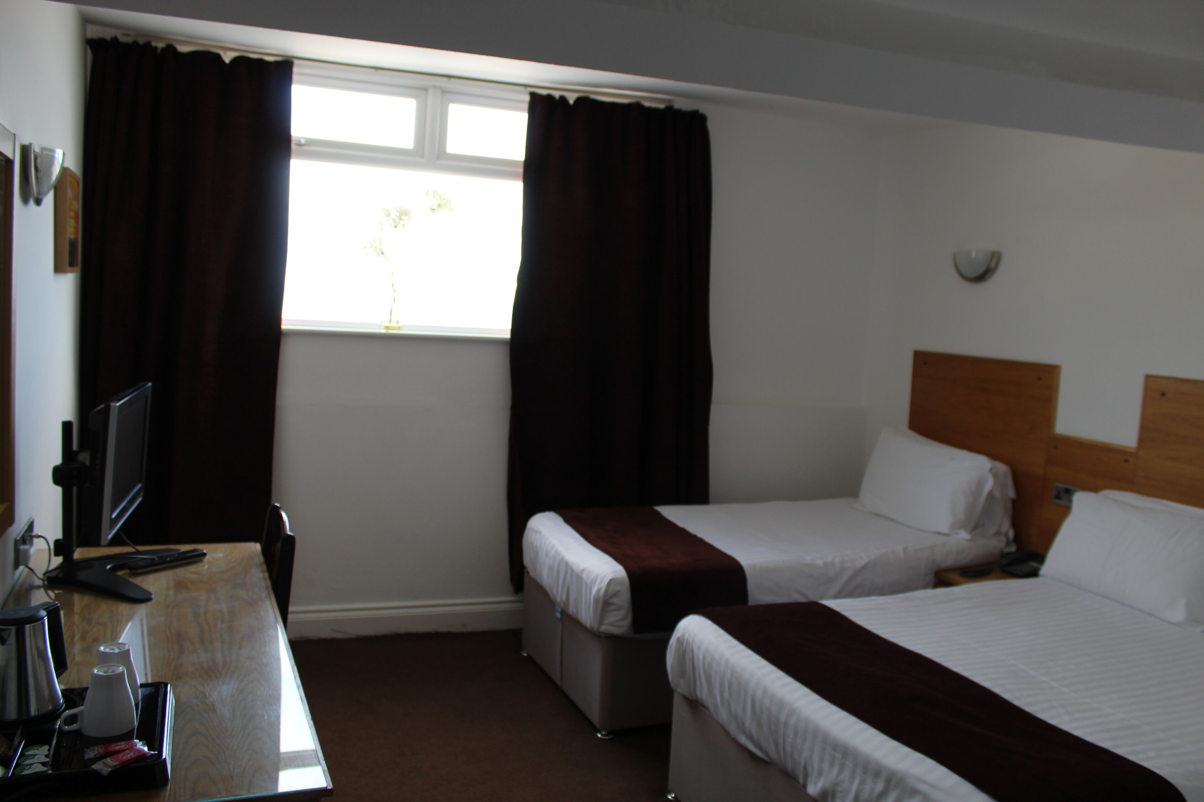 A hotel room with two single beds, a desk with a computer and coffee maker, and a window with curtains.