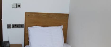 A neatly made bed with a white pillow and a dark brown blanket, a wooden nightstand with a phone, and a wall-mounted light fixture.