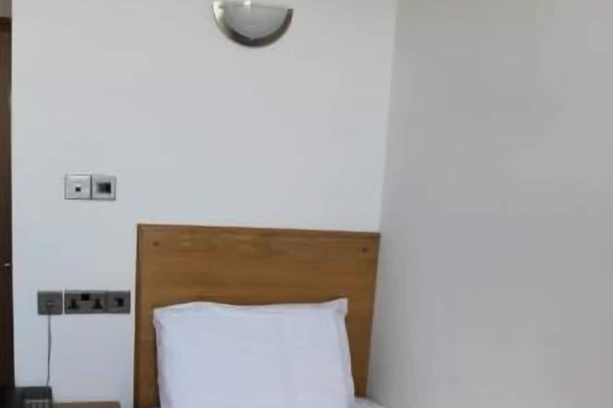 Una cama individual con cabecera de madera, una mesita de noche y una lámpara de pared.