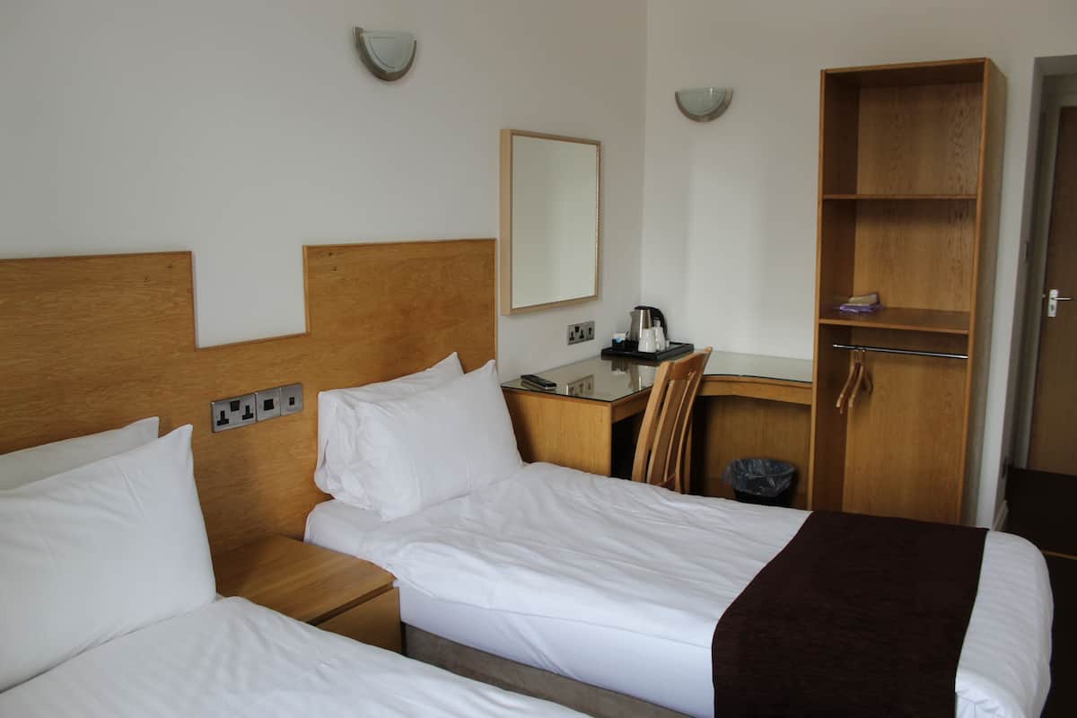 A hotel room with two beds, a desk, a chair, a mirror, and a wardrobe.