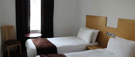 Een hotelkamer met twee bedden, een houten hoofdbord, een tafeltje, een stoel en een raam met gordijnen.