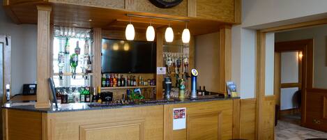 A bar area with wooden paneling, a mounted sign, and a variety of bottles and glasses on shelves.