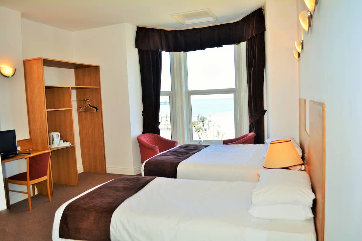 A hotel room with two beds, a desk, a chair, and a wardrobe.