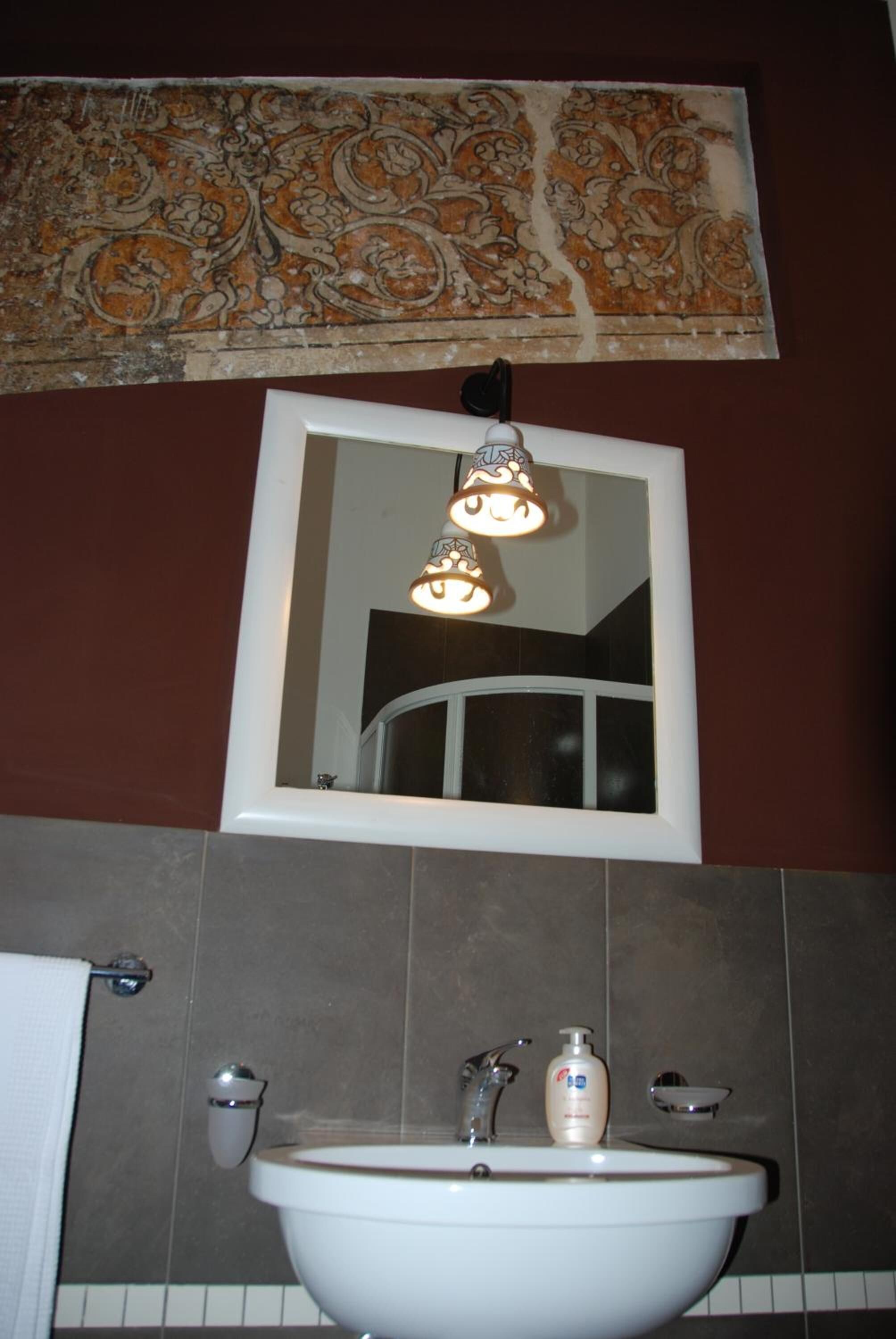 A bathroom with a white sink, a mirror, and a decorative wall piece above the mirror.