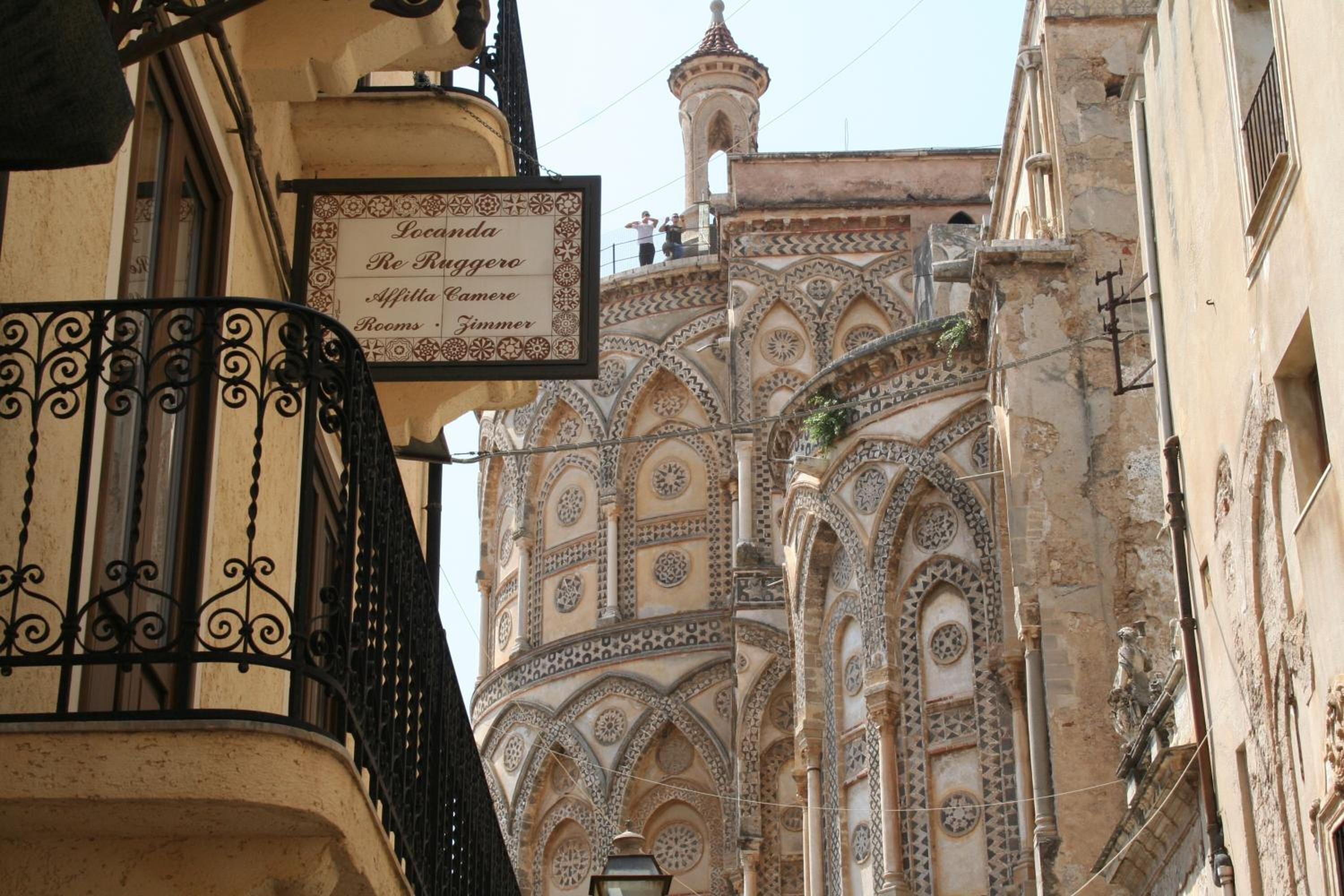 A building with ornate architectural details and a sign indicating "Locanda Re Ruggiero" with "Affitta Camera" and "Rooms" listed.