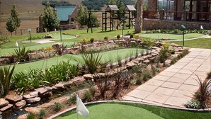 Un campo de golf con un edificio de piedra, un estanque y vistas a colinas.