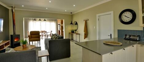 A modern kitchen with a central island, a dining area with a sofa and chairs, and a living room with a fireplace.
