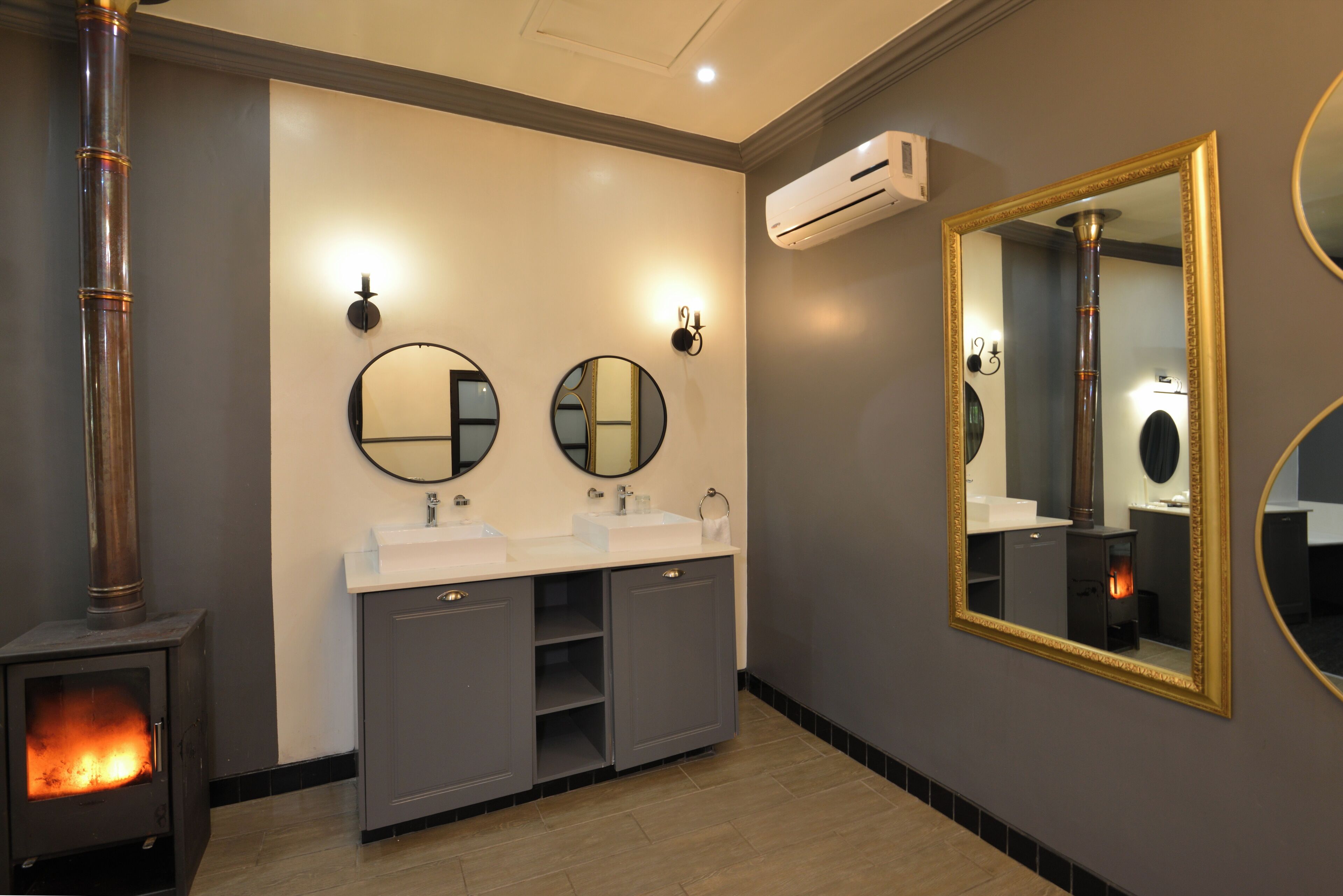 A bathroom with a wood-burning stove, two sinks, and three mirrors.