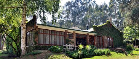 A house with a brick facade, large windows, and a garden with various plants and a small bridge.