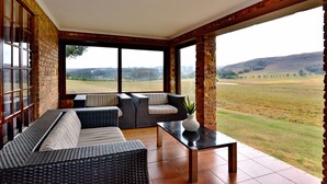 Una habitación con un ventanal amplio, muebles de mimbre y vistas a un campo.