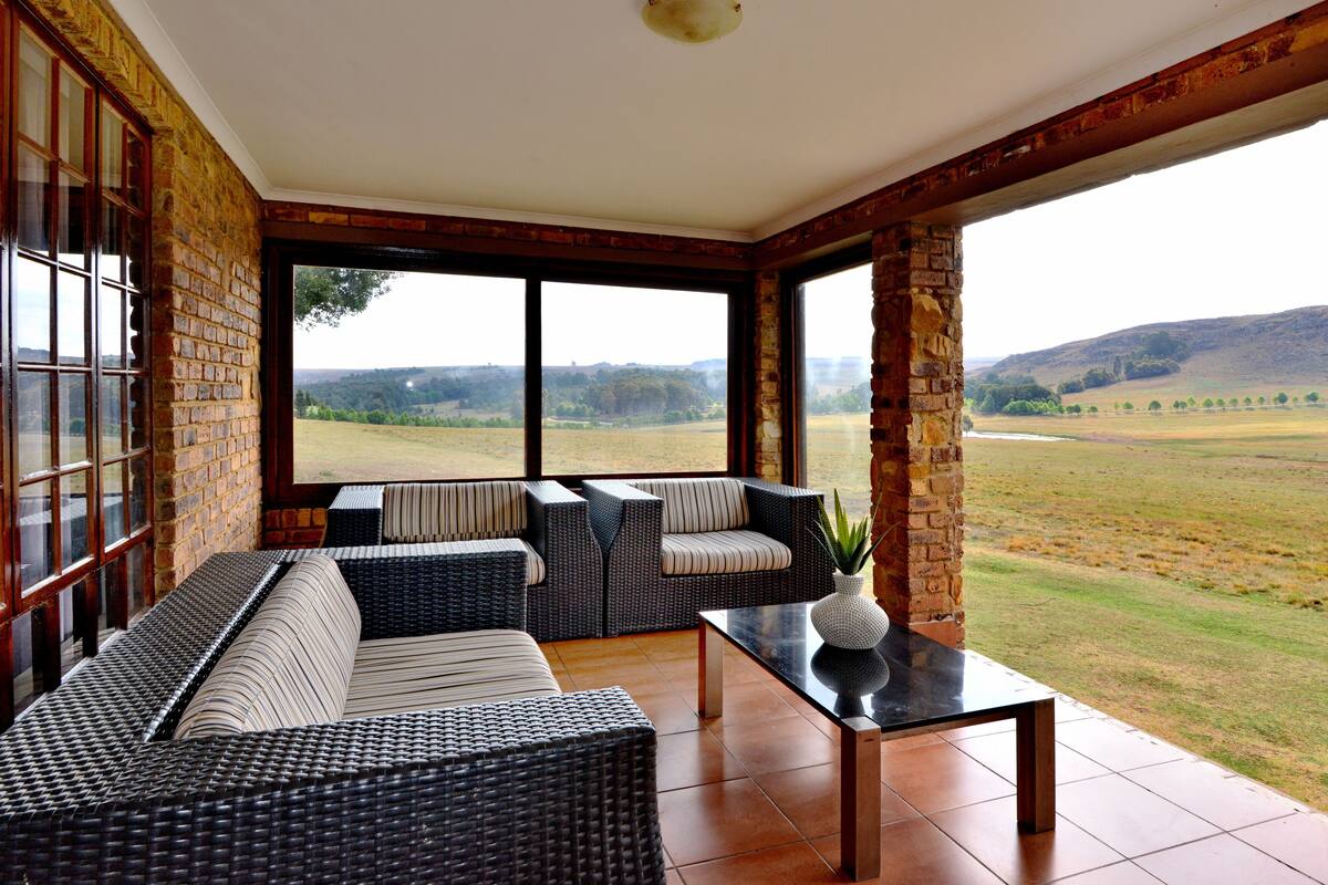 A room with a large window, wicker furniture, and a view of a field.