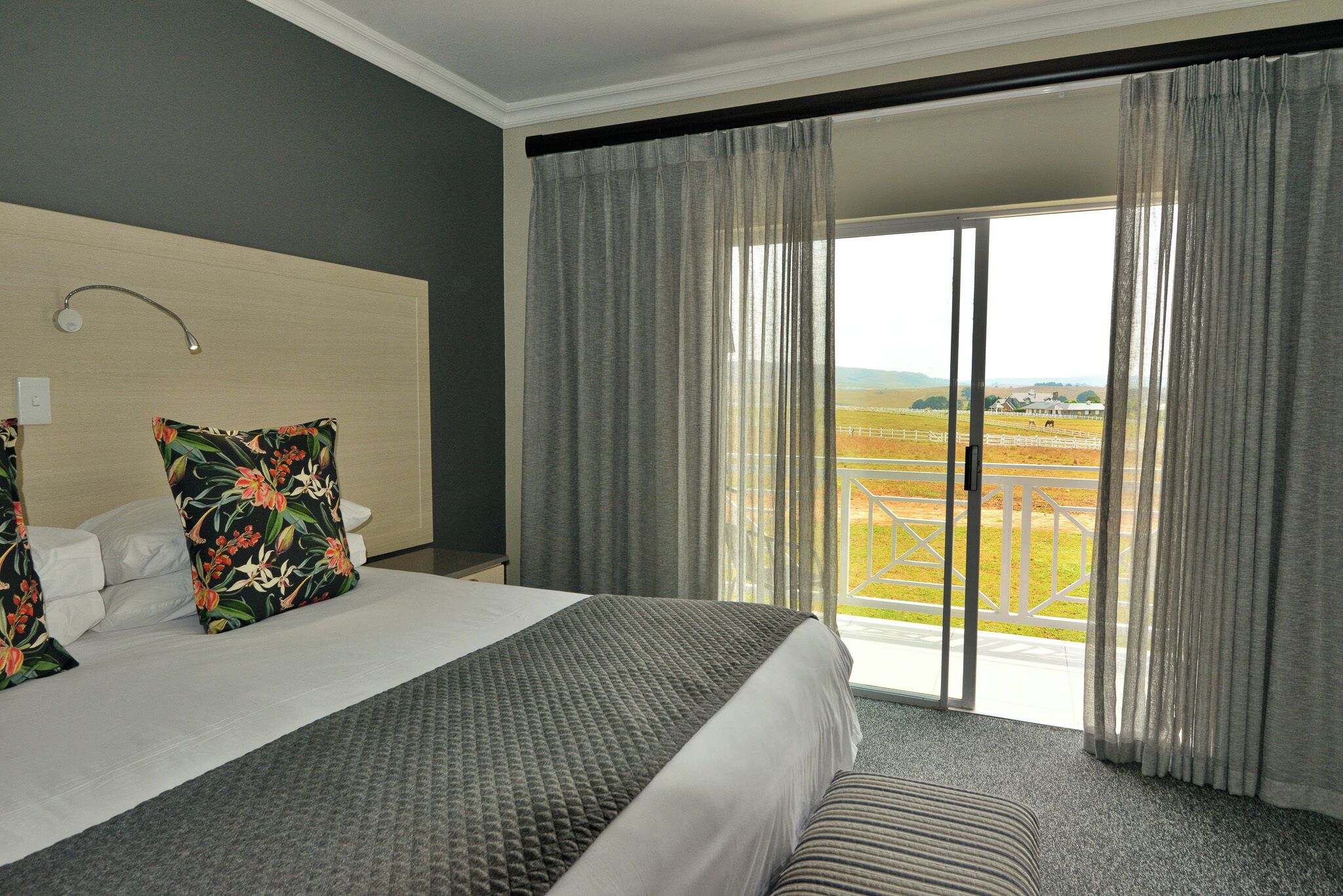 A hotel room with a large bed, a headboard, a view of a balcony with a fence, and curtains.