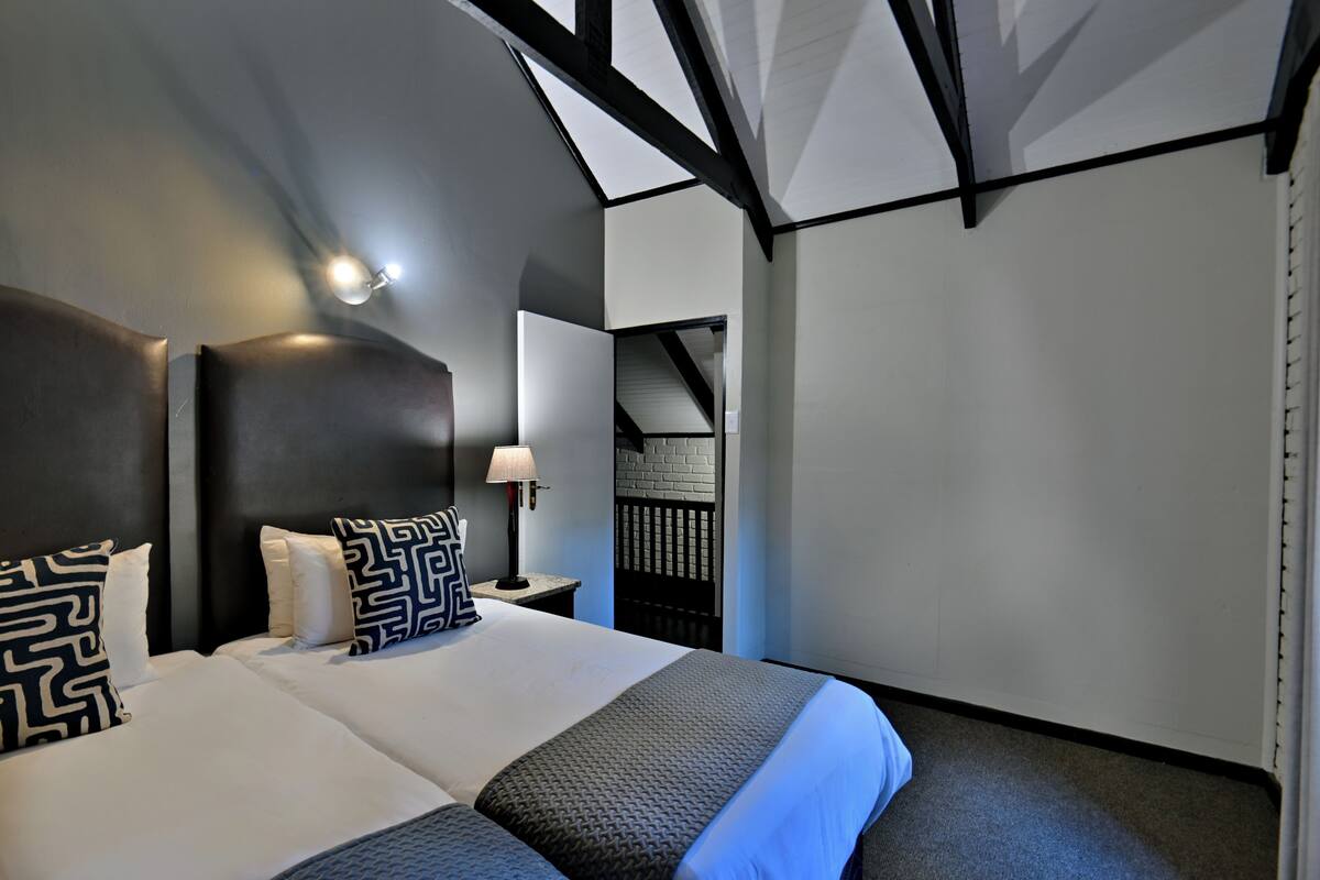 A modern hotel room with a large bed, a nightstand, a lamp, and a view of the outside.