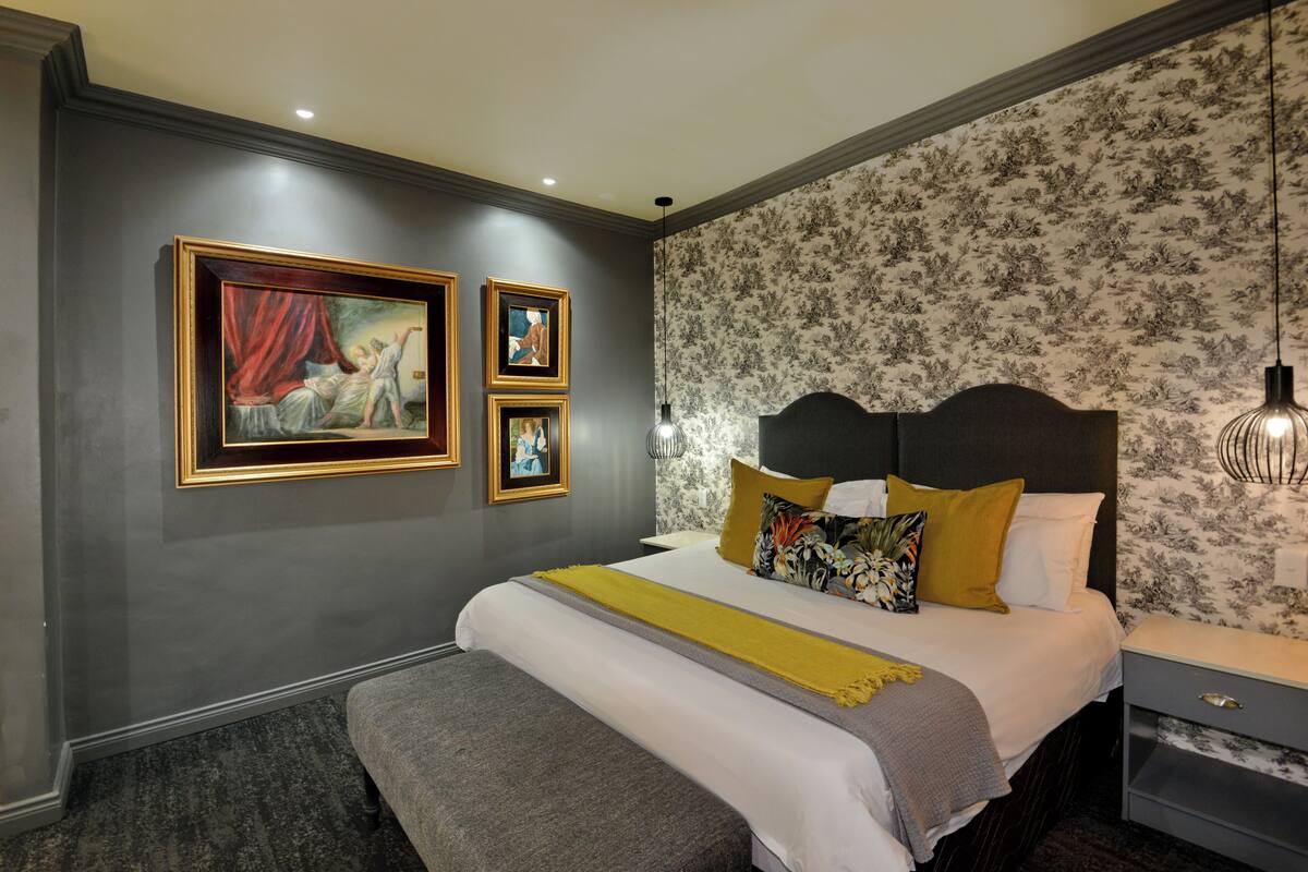 A bedroom with a large bed, a bedside table, a bench, and three framed pictures on the wall.