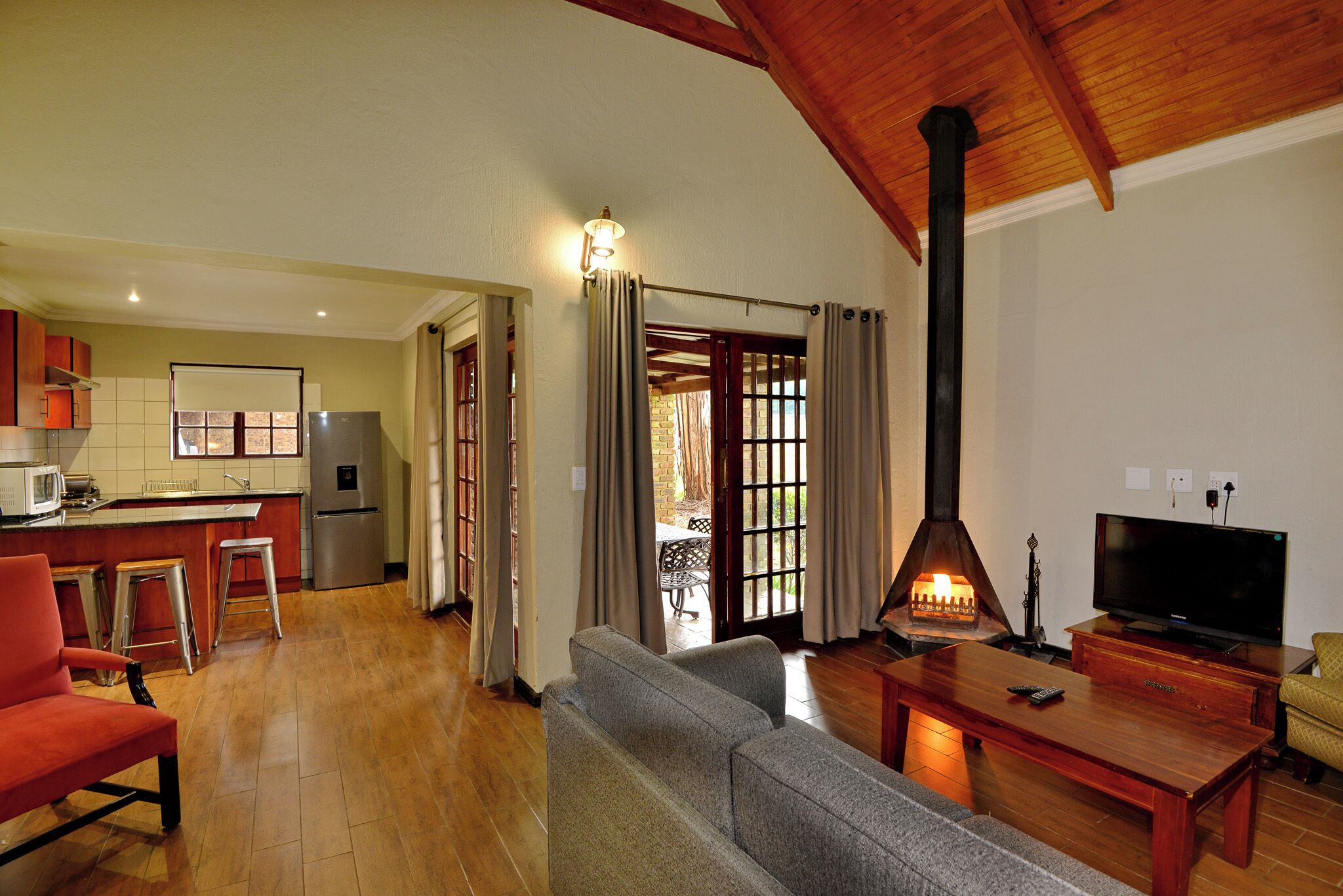 A spacious living area with a wooden ceiling, a sofa, a coffee table, a TV, and a kitchen in the background.