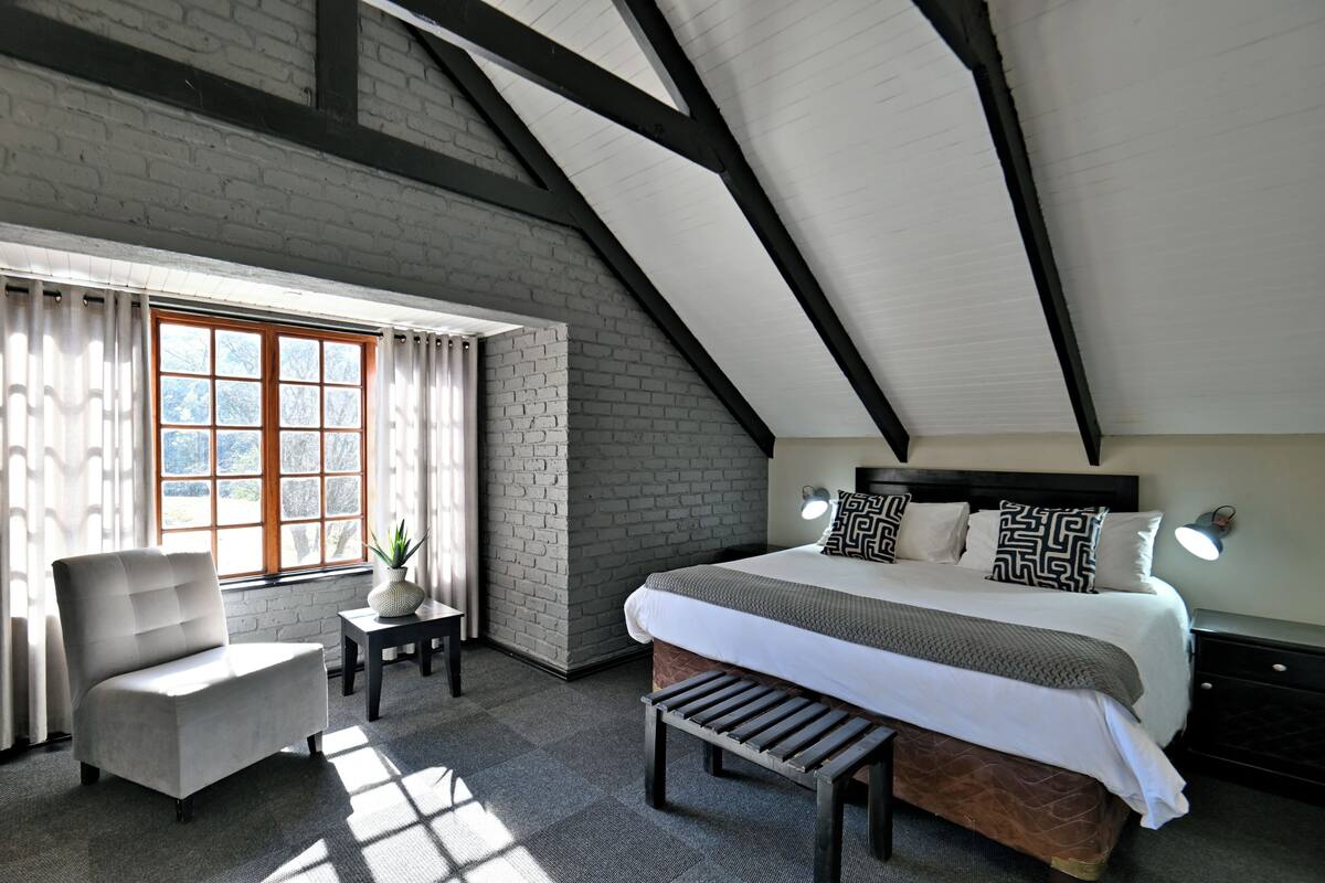 A bedroom with a large bed, a chair, a small table, and a window with curtains.