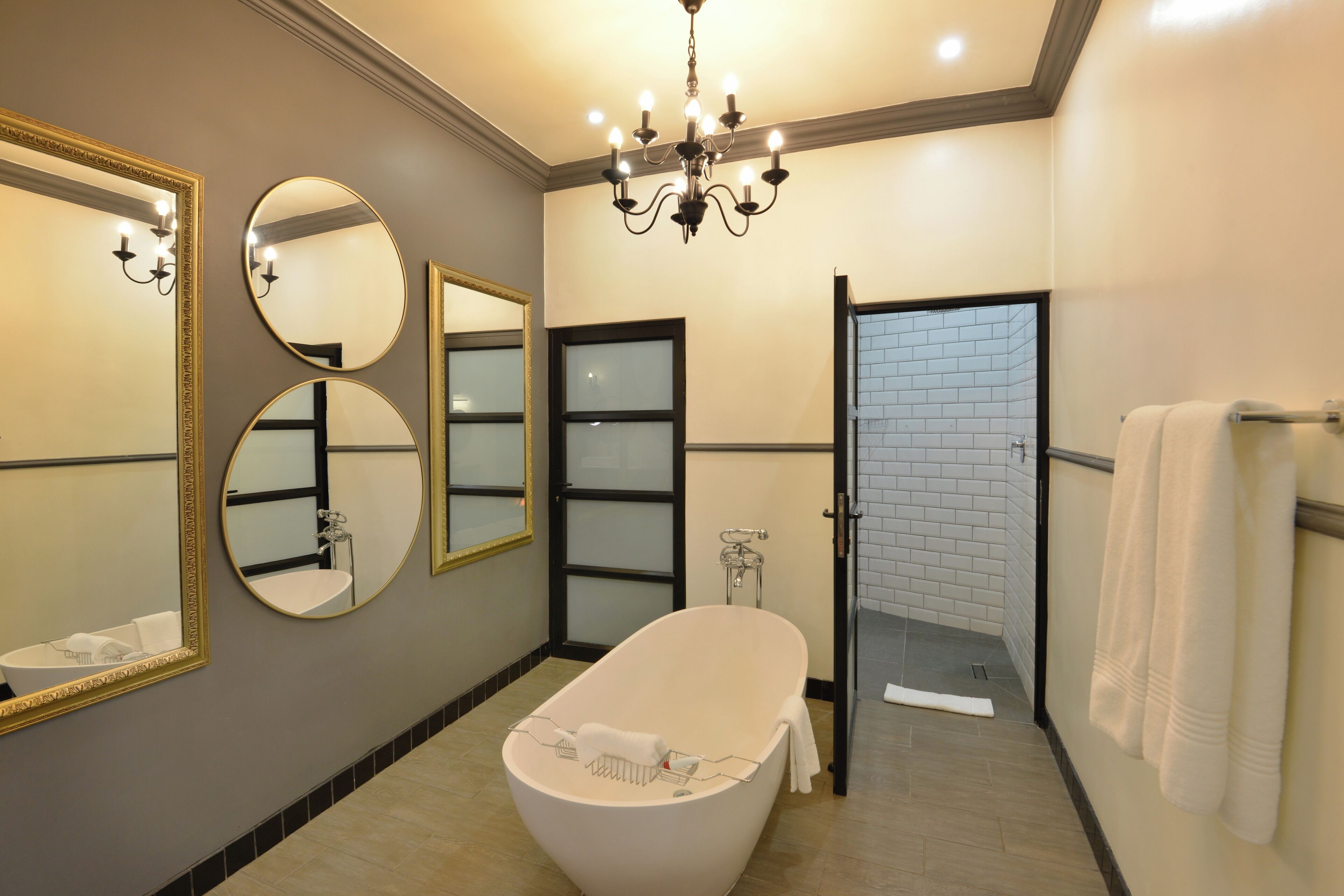A modern bathroom with a freestanding bathtub, multiple mirrors, and a chandelier.