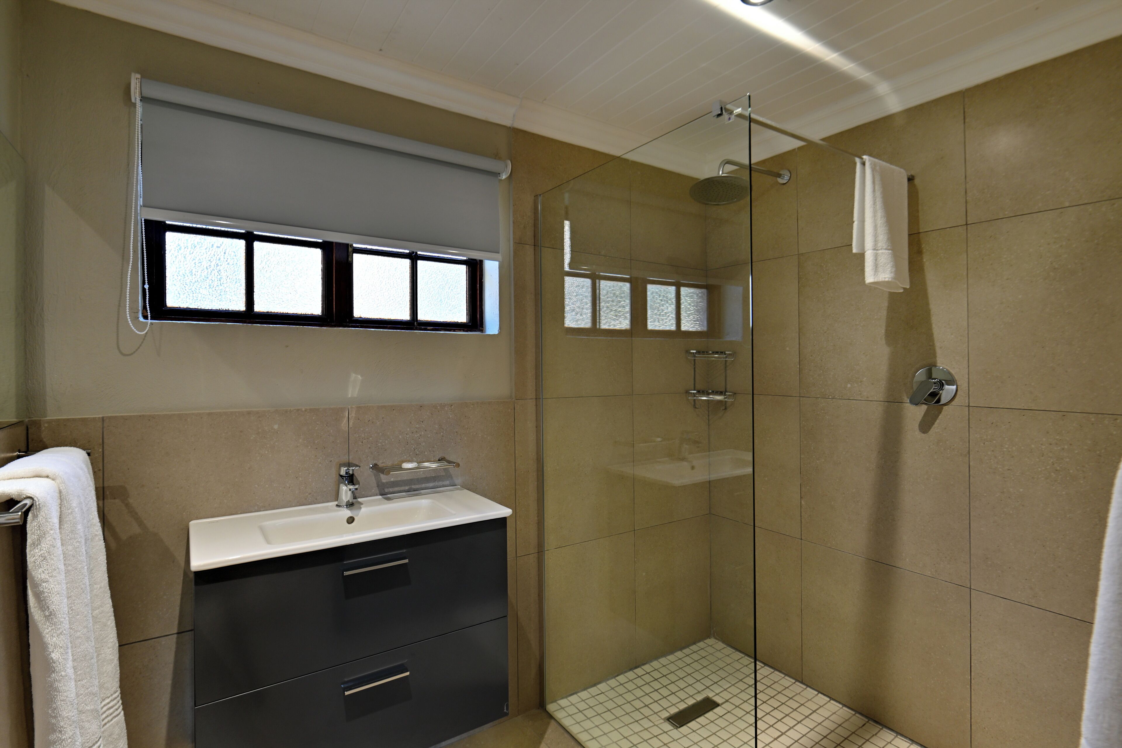 Un baño con cabina de ducha de vidrio, un lavabo con espejo y una toalla colgada en la pared.